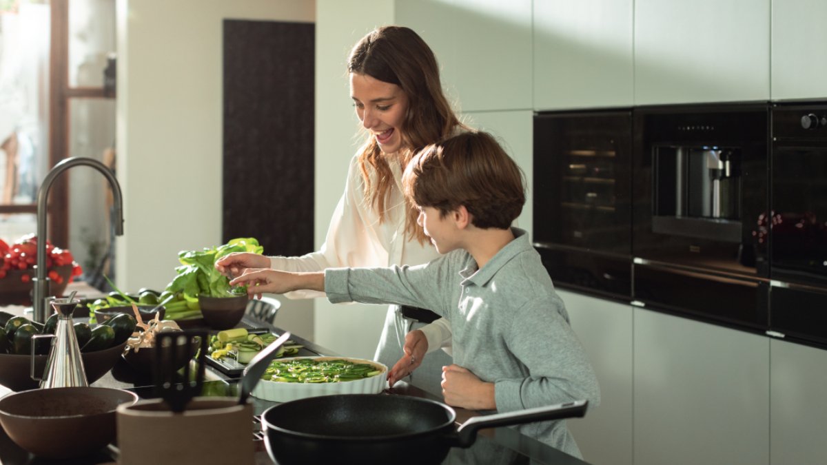 Mom and kid cooking surrounded by Franke sink, tap, microwave, oven and coffee machine.